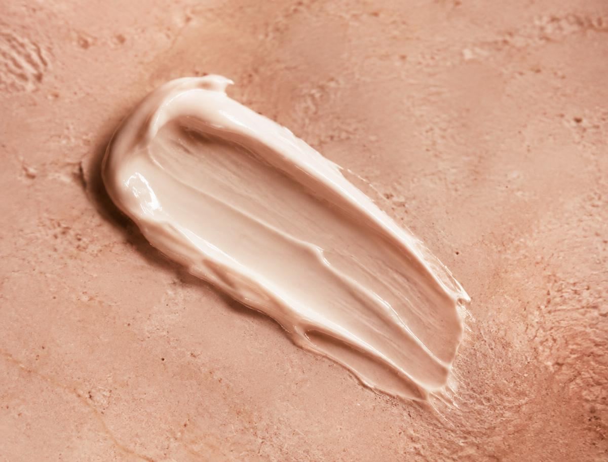 Close-up of a soft cream skincare texture on a warm nude surface